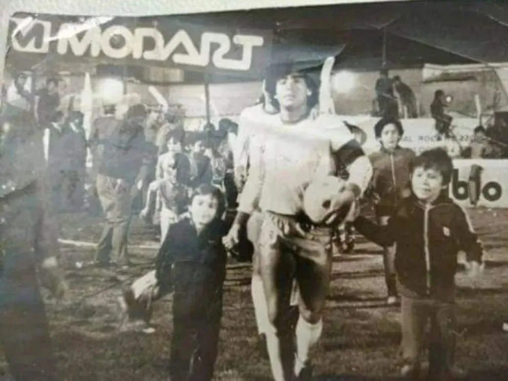 Maradona en una de sus visitas a Roca, acompañado por un niño de la ciudad. Foto: archivo histórico.